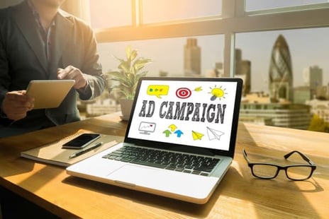 Laptop open on a desk, with the words Ad Campaign on the screen.