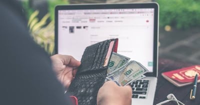 Person sitting in front of a laptop, with a wallet in their hands, pulling out money.