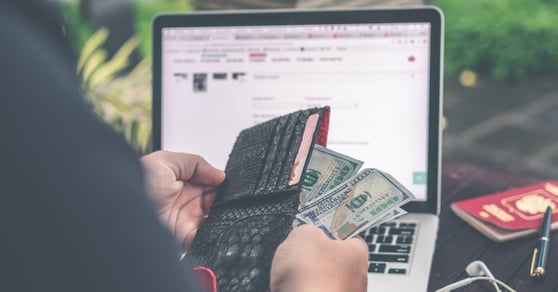 Person sitting in front of a laptop, with a wallet in their hands, pulling out money.
