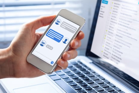 Person holding a phone with the messeging app open, in front of a laptop.