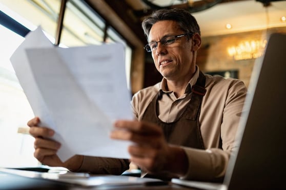Small business owner reviewing documents while learning from a guide to GA4 at his workspace.