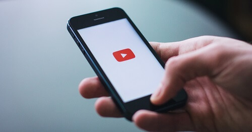 Hand holding a cell phone with the YouTube icon.